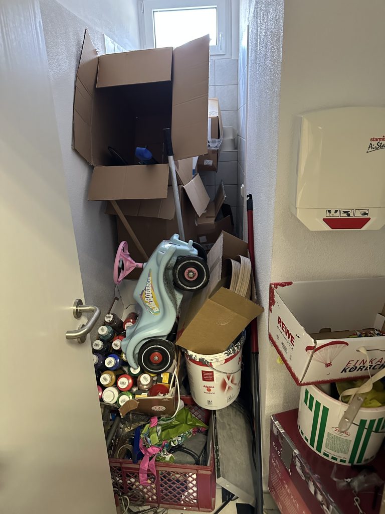 Unordentlicher Toilettenraum mit vielen Kartons, Farbeimern und Spielsachen