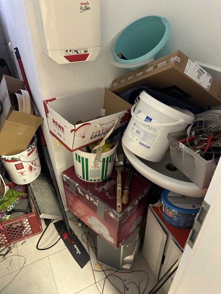Unordentlicher Waschbeckenbereich mit vielen Kartons, Farbeimern und Spielsachen